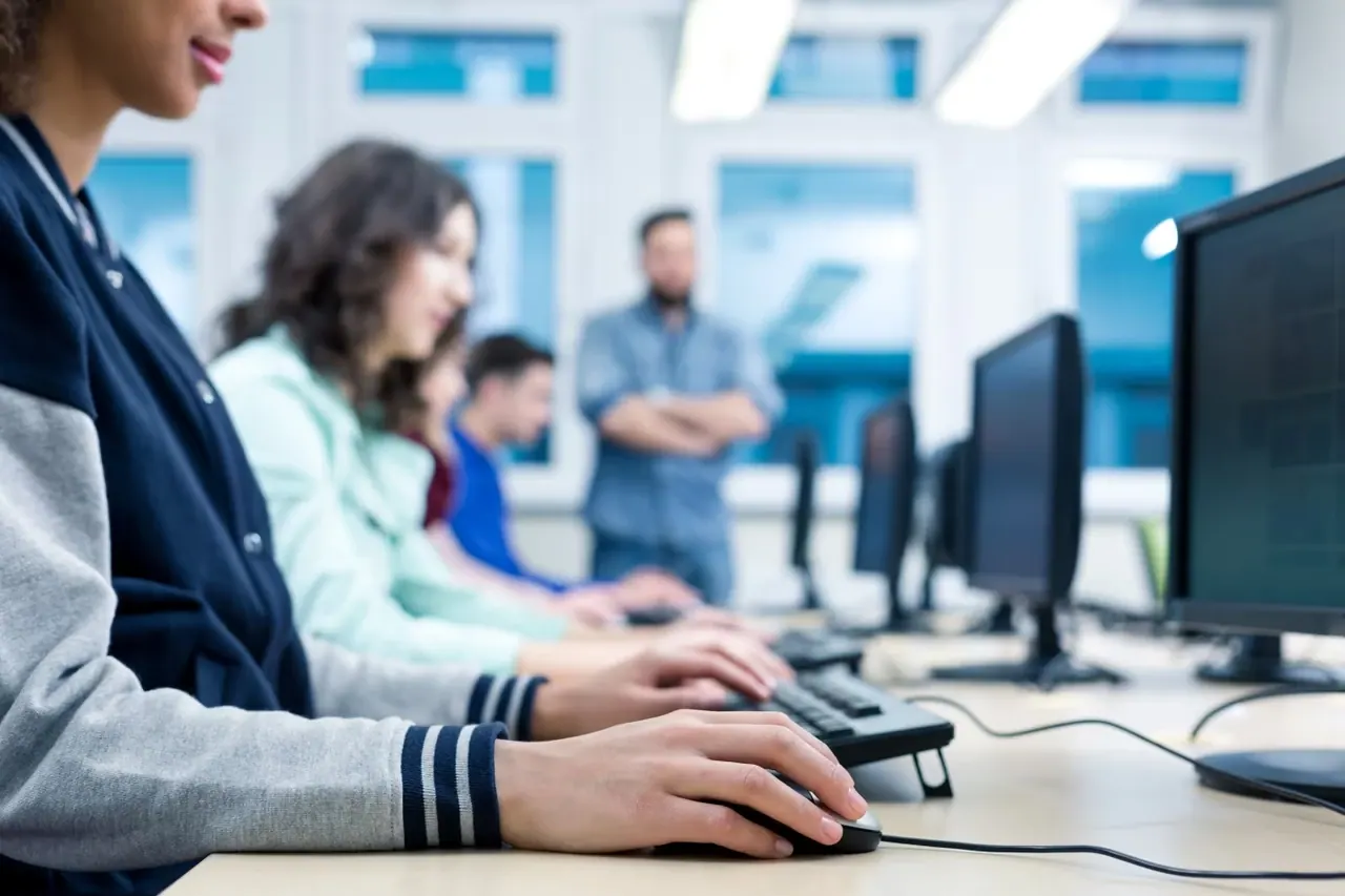 Des étudiants suivent une formation sur ordinateur, un formateur en arrière-plan