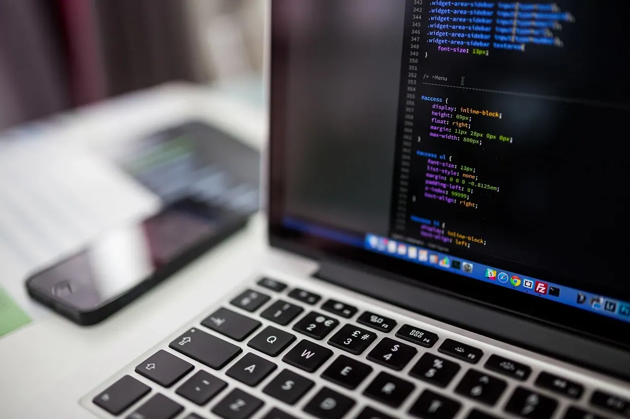 Ordinateur portable affichant du code de développement web, un smartphone au second plan